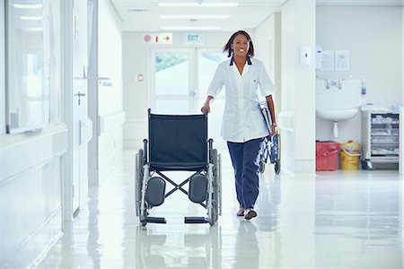 simsearch:649-08745361,k - Female orderly pushing wheelchair along hospital corridor Stock Photo - Premium Royalty-Free, Code: 649-08745348