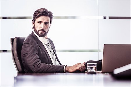 Confident businessman looking over shoulder from office desk Stock Photo - Premium Royalty-Free, Code: 649-08745573