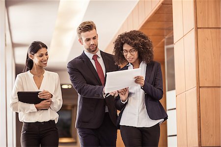 simsearch:649-08125971,k - Young businesswomen and businessman walking and reading paperwork in office corridor Foto de stock - Sin royalties Premium, Código: 649-08745597