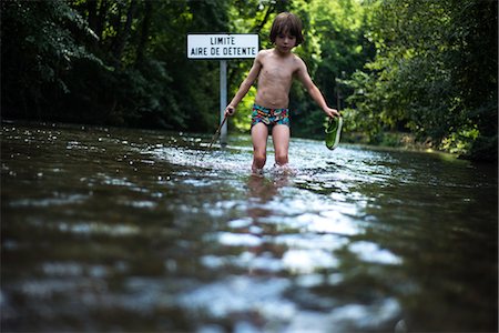 swim shorts for boys - Boy knee deep in water holding shoe, France Stock Photo - Premium Royalty-Free, Code: 649-08745636