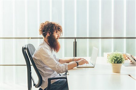 simsearch:649-08765934,k - Young male hipster with red hair and beard typing on laptop at desk Foto de stock - Sin royalties Premium, Código: 649-08765960