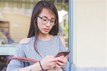 simsearch:649-09252029,k - Young woman texting on smartphone outside sidewalk cafée Fotografie stock - Premium Royalty-Free, Codice: 649-08824065