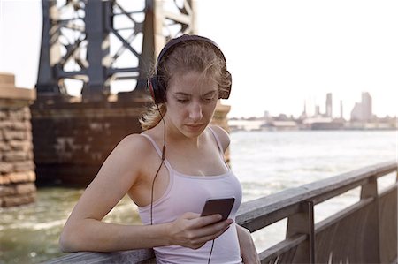 ponte williamsburg - Young woman beside river, wearing headphones, using smartphone, New York City, USA Foto de stock - Royalty Free Premium, Número: 649-08824086