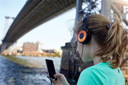 ponte williamsburg - Young woman beside river, wearing headphones, using smartphone, rear view, New York City, USA Foto de stock - Royalty Free Premium, Número: 649-08824090