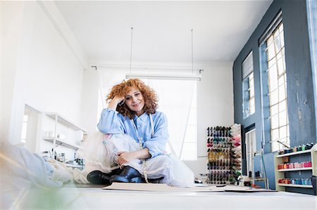 personaggio (tipo eccentrico) - Fashion designer sitting cross-legged on desk looking at camera smiling Fotografie stock - Premium Royalty-Free, Codice: 649-08824577