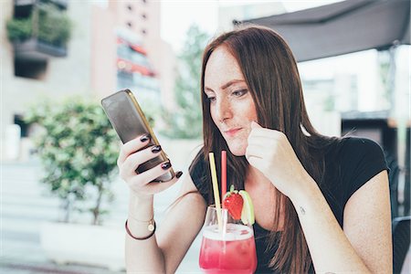 simsearch:649-08824700,k - Young woman at sidewalk cafée reading smartphone texts Foto de stock - Royalty Free Premium, Número: 649-08824700