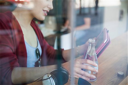 Young woman sitting in cafée, holding bottle of water, using digital tablet Photographie de stock - Premium Libres de Droits, Code: 649-08824737