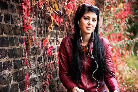 Portrait of young woman sitting outdoors, wearing earphones Stock Photo - Premium Royalty-Free, Code: 649-08824883
