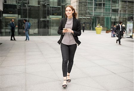 Woman walking in city holding smartphone Stock Photo - Premium Royalty-Free, Code: 649-08825006