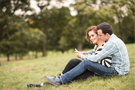 simsearch:614-08392622,k - Couple sitting in field hugging looking at smartphone Photographie de stock - Premium Libres de Droits, Code: 649-08825056