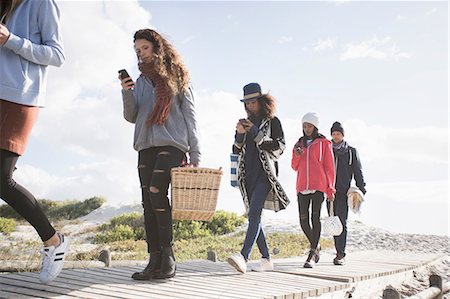 simsearch:649-08118646,k - Row of young adult friends strolling along beach boardwalk reading smartphones, Western Cape, South Africa Stock Photo - Premium Royalty-Free, Code: 649-08840220