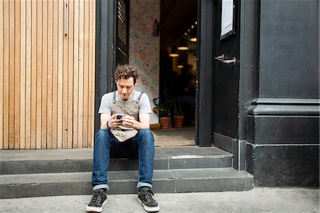 simsearch:614-08827243,k - Waiter taking a break on cafe step looking at smartphone Stock Photo - Premium Royalty-Free, Code: 649-08840246