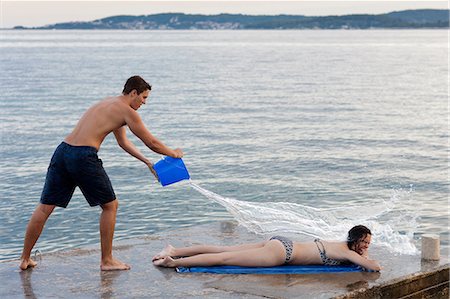 Young man throwing bucket of water over female sunbather, Orebic, Croatia Foto de stock - Sin royalties Premium, Código: 649-08859924