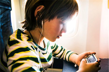 simsearch:649-08860216,k - Boy on airplane selecting music on mp3 player Fotografie stock - Premium Royalty-Free, Codice: 649-08860215