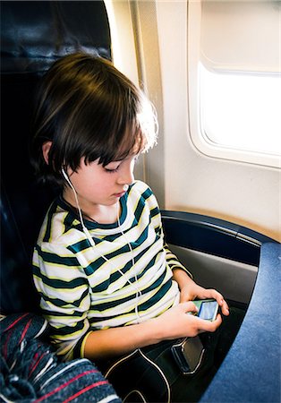 Boy on airplane selecting music on mp3 player Stock Photo - Premium Royalty-Free, Code: 649-08860219