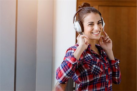 Portrait of young woman in plaid shirt in corridor listening to headphones Stock Photo - Premium Royalty-Free, Code: 649-08860345