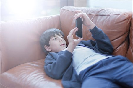 Boy playing with smartphone on sofa Fotografie stock - Premium Royalty-Free, Codice: 649-08894002