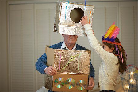 simsearch:649-08894043,k - Girl in feather headdress putting robot costume onto grandfather Stock Photo - Premium Royalty-Free, Code: 649-08894044