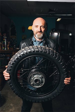 simsearch:649-08894214,k - Portrait of mature man, in garage, holding motorcycle tire Foto de stock - Sin royalties Premium, Código: 649-08894212