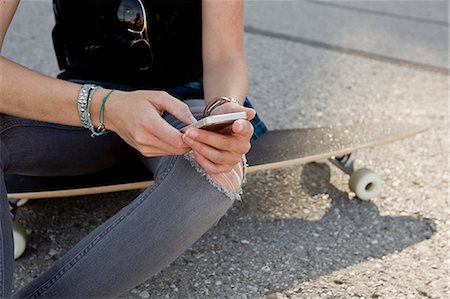 simsearch:649-09036191,k - Mid section of female skateboarder sitting on skateboard texting on smartphone Stock Photo - Premium Royalty-Free, Code: 649-08894249