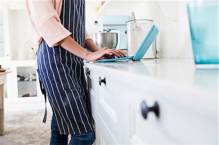 Mid section of young female baker at kitchen counter typing on laptop Stock Photo - Premium Royalty-Free, Code: 649-08894285