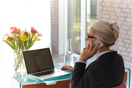 simsearch:614-08578376,k - Senior businesswoman using laptop and making smartphone call at home desk Fotografie stock - Premium Royalty-Free, Codice: 649-08894598