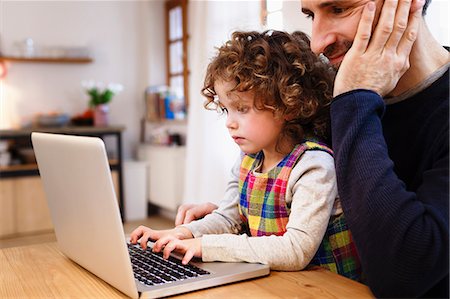 suéters - Girl on father's lap typing on laptop in kitchen Foto de stock - Sin royalties Premium, Código: 649-08894904