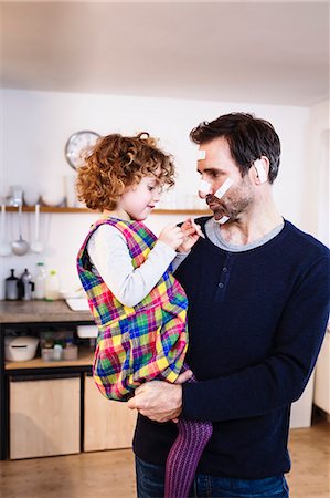 family playing in the kitchen - Girl sticking adhesive plasters onto father's face Stock Photo - Premium Royalty-Free, Code: 649-08894900