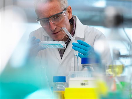 person in white coat and goggles - Biotechnology Research, scientist viewing samples in a multi well plate during an experiment in the laboratory Stock Photo - Premium Royalty-Free, Code: 649-08894944