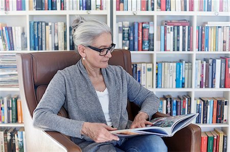 simsearch:614-08881367,k - Senior woman sitting in chair in library, reading book Photographie de stock - Premium Libres de Droits, Code: 649-08900654