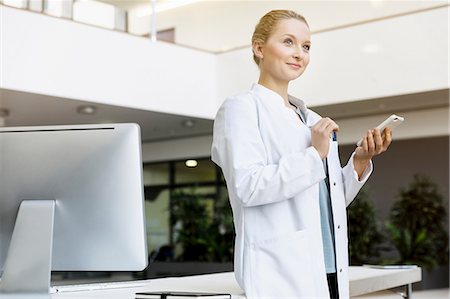 Doctor standing beside computer, holding smartphone Stock Photo - Premium Royalty-Free, Code: 649-08900678