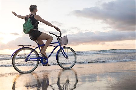 Woman waving while cycling on beach at sunset, Nosara, Guanacaste Province, Costa Rica Stock Photo - Premium Royalty-Free, Code: 649-08900719