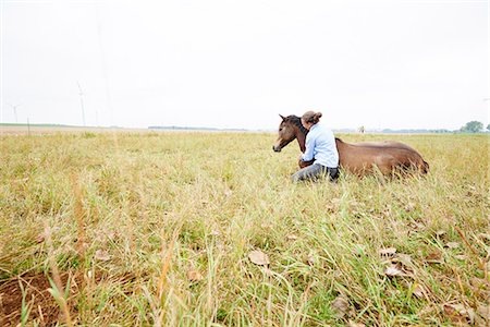 Woman crouching with arm around horse lying down in field Photographie de stock - Premium Libres de Droits, Code: 649-08900810