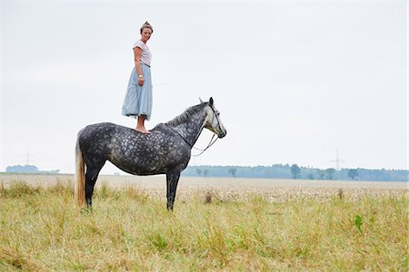 Woman in skirt standing on top of dapple grey horse in field Photographie de stock - Premium Libres de Droits, Code: 649-08900821