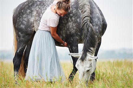 Woman in skirt with arms around dapple grey horse in field Stock Photo - Premium Royalty-Free, Code: 649-08900822