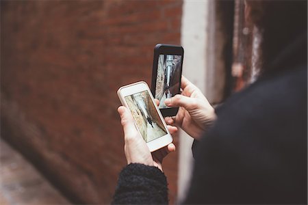 Over the shoulder view of man holding two smartphones with photographs of alley, Venice, Italy Stock Photo - Premium Royalty-Free, Code: 649-08900848