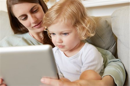 Female toddler sitting on mother's knee looking at digital tablet Stock Photo - Premium Royalty-Free, Code: 649-08901023