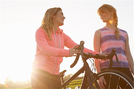 Female cyclists strolling with racing cycle in sunlit park Stock Photo - Premium Royalty-Free, Code: 649-08901510