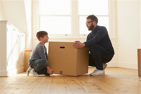 Mid adult man and son crouching to lift cardboard box in new home Foto de stock - Sin royalties Premium, Código: 649-08901549