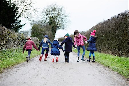 Rear view of boy and girls holding hands and fooling around on rural road Stock Photo - Premium Royalty-Free, Code: 649-08901585