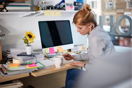 simsearch:649-08902016,k - Woman sitting at desk in office writing on notepad Photographie de stock - Premium Libres de Droits, Code: 649-08902045
