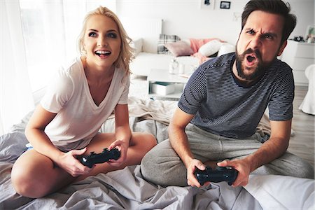 pajamas video game pictures - Couple sitting on bed, holding computer controllers, playing computer game Stock Photo - Premium Royalty-Free, Code: 649-08902134