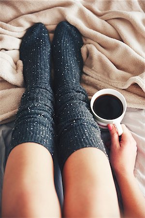 Woman sitting on bed, wearing warm socks, holding cup of coffee, low section, overhead view Stock Photo - Premium Royalty-Free, Code: 649-08902146