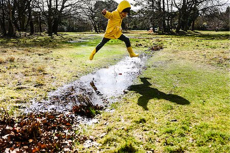 rain boots - Boy in yellow anorak jumping over puddle in park Stock Photo - Premium Royalty-Free, Code: 649-08902282