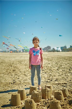 Portrait of young girl standing behind sand castles on beach, Rimini, italy Stock Photo - Premium Royalty-Free, Code: 649-08924701