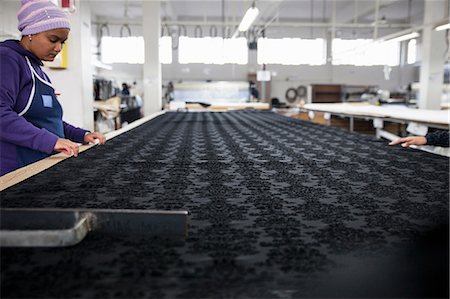 Factory workers smoothing black patterned textile on work table in clothing factory Photographie de stock - Premium Libres de Droits, Code: 649-08922790