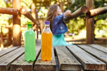 Teenage girl leaning on climbing frame at park, two bottled soft drinks in foreground Stock Photo - Premium Royalty-Free, Code: 649-08922952