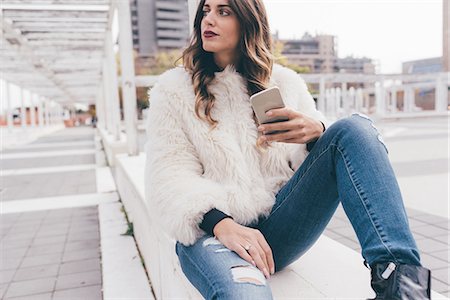 simsearch:649-08923095,k - Young woman sitting outdoors, holding smartphone, looking away Foto de stock - Royalty Free Premium, Número: 649-08923055