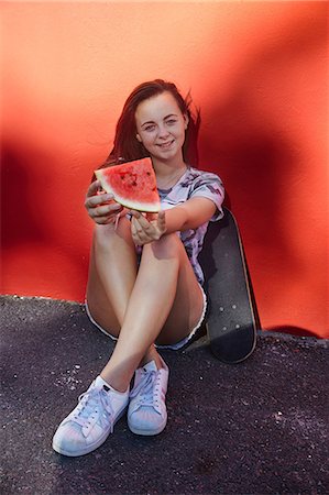 Teenage girl with watermelon and skateboard, red wall in background Stock Photo - Premium Royalty-Free, Code: 649-08923583