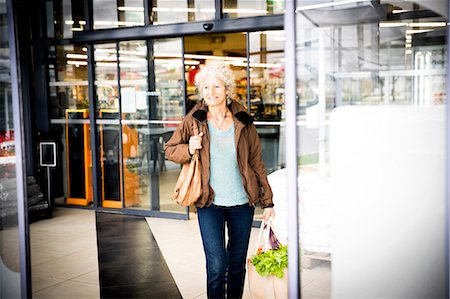 Mature woman exiting supermarket with bag of shopping Stock Photo - Premium Royalty-Free, Code: 649-08923765